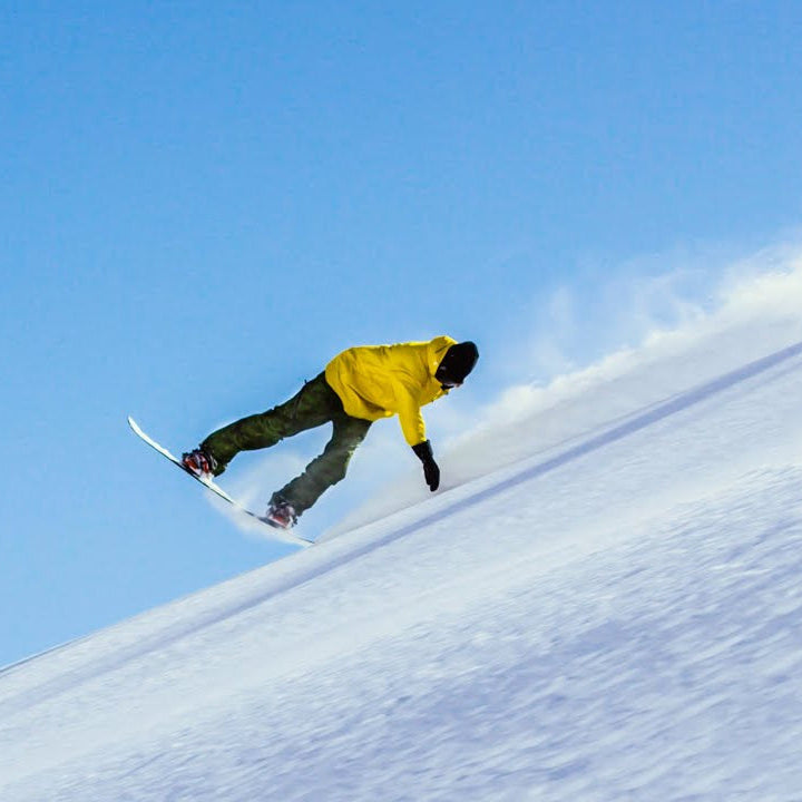 Person snowboarding down a snowy slope with a clear blue sky